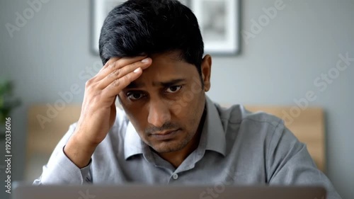 Focused indian man looking stressed while working on laptop computer