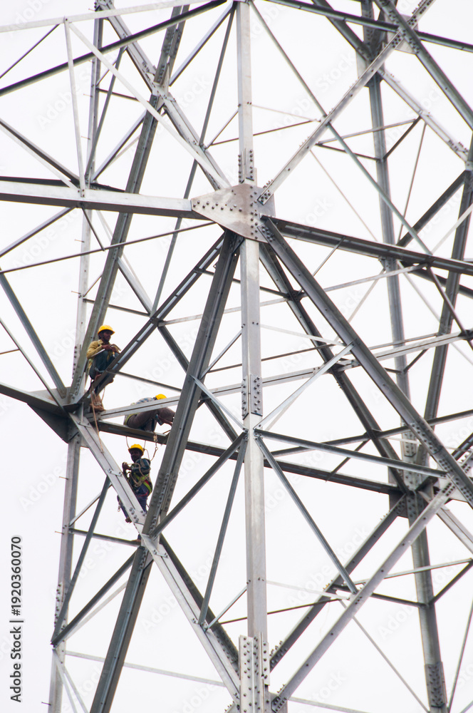 Fototapeta premium Pylon construction workers working on the top of power tower.