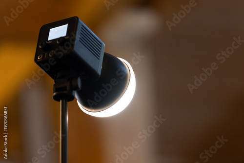 Wallpaper Mural Close-up of a studio lamp spotlight emitting a warm LED glow on an adjustable stand, used for photography and video lighting in an indoor setting to create mood, texture, and contrast Torontodigital.ca