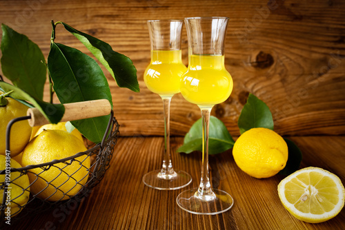 Limoncello in two glasses with ripe lemons on a rustic wooden base. Italian liqueur.