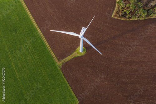 Aerial view of a solitary wind turbine stands in stark contrast against the patchwork of vibrant green fields and rich brown soil, Plozevet, Brittany, France.