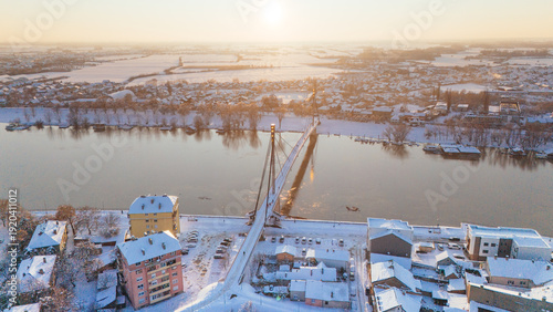 Aerial view of a snow-dusted bridge spanning the glimmering river, casting long shadows over the cityscape, Sremska Mitrovica, Vojvodina, Serbia.