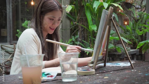 Happy young adult asian woman painting brush on canvas at workshop art lesson class outdoor cafe creativity hobby