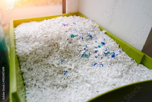 Foto White shredded plastic flakes, mixed with blue and green pieces, fill a bright g