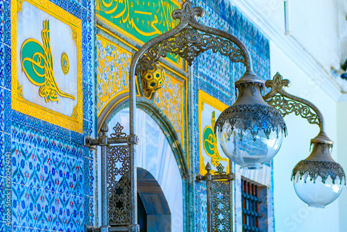 Decorative facade of Topkapi Palace in Istanbul in soft focus featuring intricate Ottoman Iznik tiles, golden Sultan's Tughra calligraphy, and vintage wrought iron lantern.
