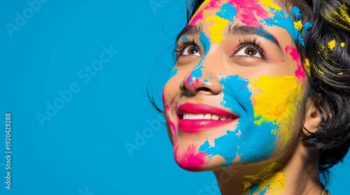 A young Hispanic woman with short black hair has her face painted in bright colors, including blue, pink, and yellow, against a solid blue background.