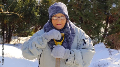 Portrait of an elderly woman with a snow shovel in winter. An old woman removes snow with a shovel in winter.