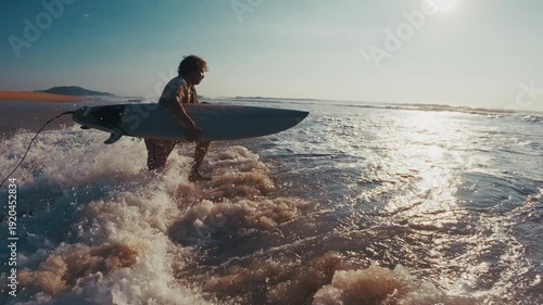 Stylish surfer. Young man in bright colorful shirt walks with surfing board on the sandy beach and enters the water