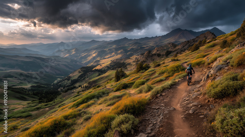 a cyclist in the mountains under a heavy cloudy sky. Male tourist biking along grassy trail in the mountains, wearing helmet and backpack.
