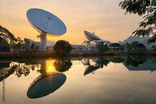Bild auf Leinwand Satellite dish antenna station with reflection on pond at sunrise