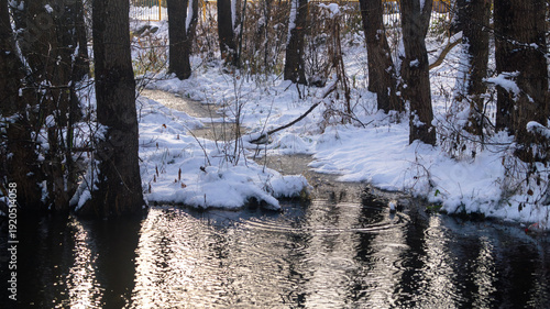 A small stream in a snowy forest. A small river in a snowy forest with glints on the surface and snow-covered banks