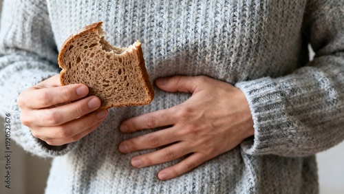 Person holding a bitten slice of bread while clutching their stomach, indicating discomfort from a potential digestive issue.