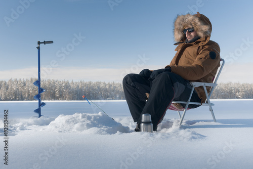 A man sits on a chair and waits intently for a bite while ice fishing.