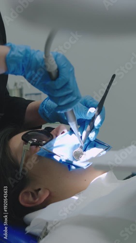Patient receives dental treatment in a clinic while dentist checks teeth and performs a procedure during a routine checkup