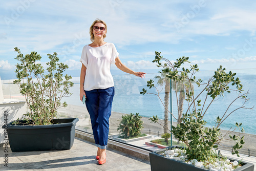 Woman traveler looking at camera enjoying the sun, admire seacoast view and breathing fresh sea air in hotel terrace.