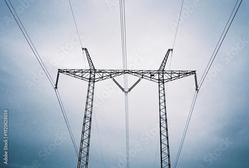 Symmetrical high voltage electricity pylon against a cloudy sky, analog photography