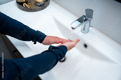 Close up of male hands washing with soap in clean white minimalistic porcelain sink. Daily hygiene routine: Person washing hands in a bright modern bathroom interior.