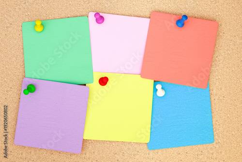 Colorful assortment of pinned sticky notes on cork board background. Organizational aids for reminders and tasks, perfect for office or educational use. Simple and effective method for notes