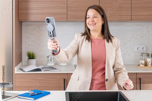 Woman holding a smartphone on a gimbal, filming a modern kitchen interior for business