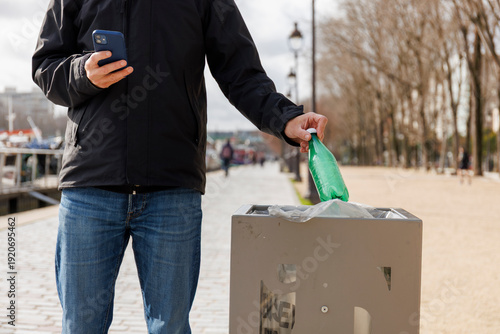 Un homme jette une bouteille plastique dans une poubelle en ville