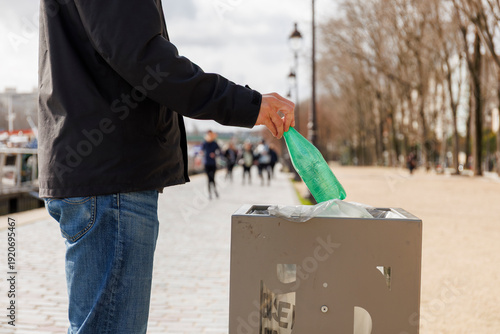Un homme jette une bouteille plastique dans une poubelle en ville