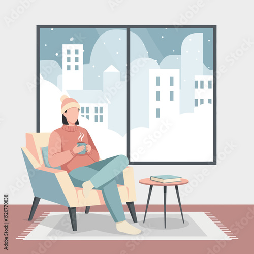 Person sitting in armchair with a hot drink during winter snowfall outside.
