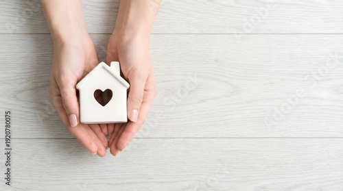 Top view of caring hands presenting miniature house symbol with heart cutout, expressing property security, mortgage coverage, emotional safety, and stable housing investment.