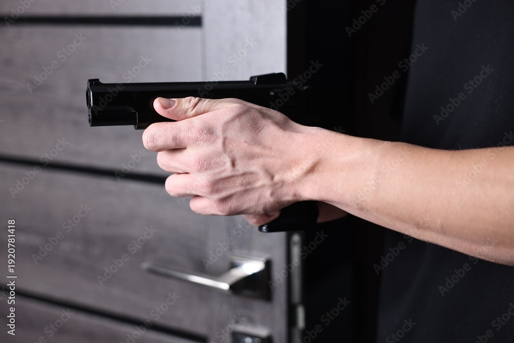 Naklejka premium Dangerous criminal holding gun indoors, closeup. Armed robbery