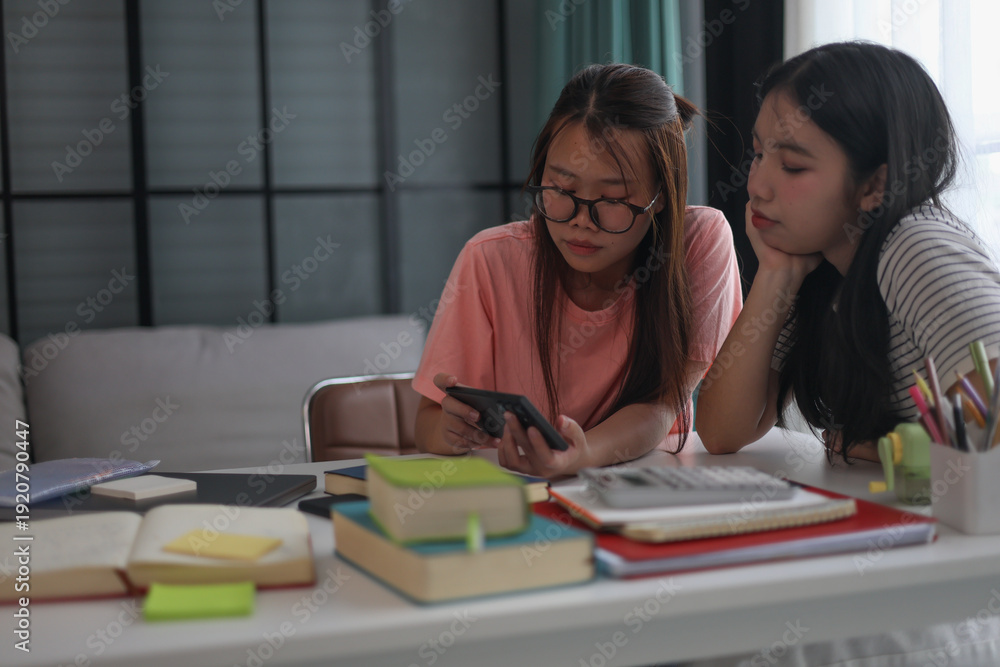 Obraz premium Two female students using smartphone during studying at home.