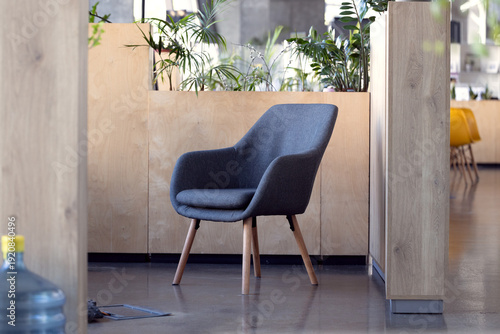Modern gray armchair with wooden legs in a contemporary office space with plants