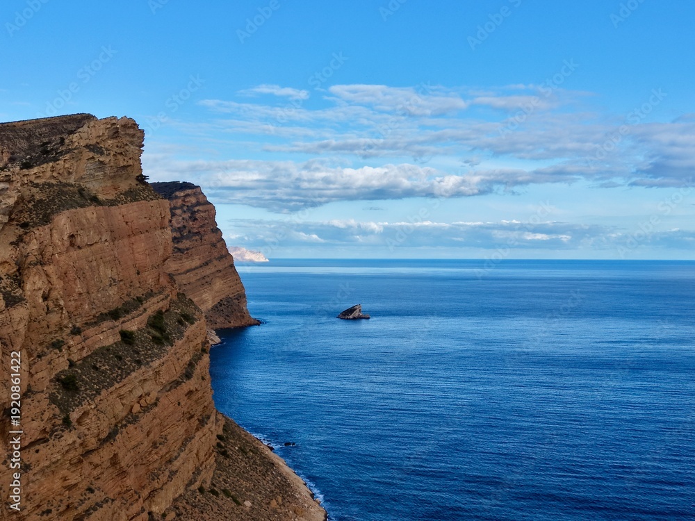 Fototapeta premium Isolation among high rocks and calm waters, Lonely artwork situated on jagged cliffs over peaceful ocean