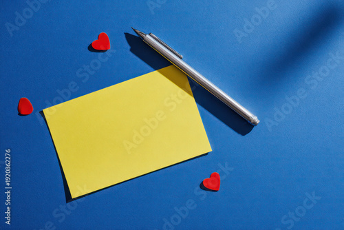 Yellow Sticky Note with Silver Pen and Red Hearts on Blue Background