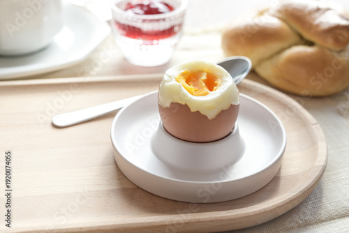 Opened boiled egg with soft yolk in an egg cup on a wooden plate, delicious protein for breakfast, brunch, or lunch, copy space, selected focus