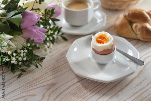 Boiled egg with soft yolk on an wooden breakfast table with buns, coffee and flowers, easter or mothers day, copy space, selected focus