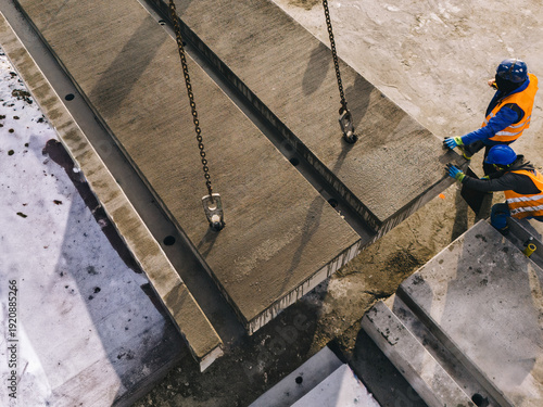 Installation of large prefabricated concrete slabs at an active construction site. Workers guiding heavy precast elements during an industrial assembly process.