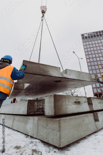 Workers installing a large prefabricated concrete slab using a crane at an urban construction site. Teamwork and heavy machinery ensure precise placement of precast elements.