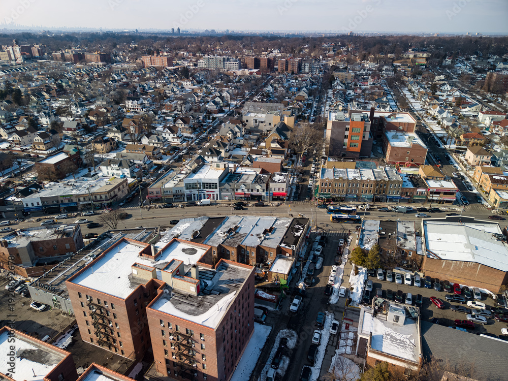 Fototapeta premium Aerial view showcasing a typical hollis, queens, new york neighborhood with residential homes, commercial buildings, and streets covered in light snow during winter