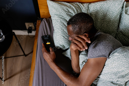 Top view of adult black man turning off alarm on smartphone in bed