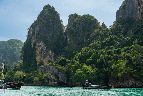 Long-tail boat speeding through turquoise water past jungle cliffs near Railay Beach