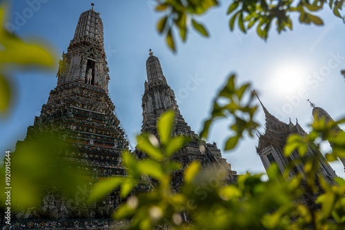 Slika na platnu Sunlit Prang towers of Wat Arun framed by lush green foliage, Bangkok