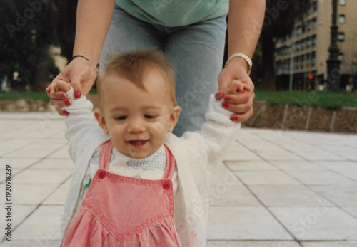 A baby girl is learning how to walk with a little help of her mother