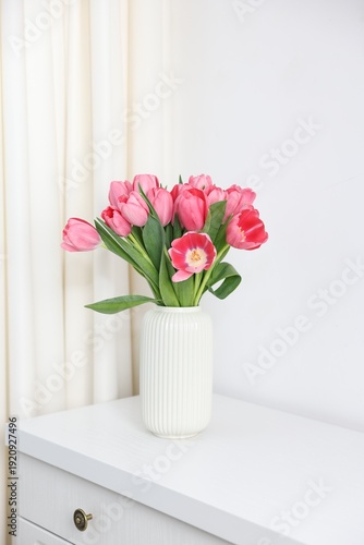 Bouquet of pink tulips in vase on chest of drawers near white wall indoors