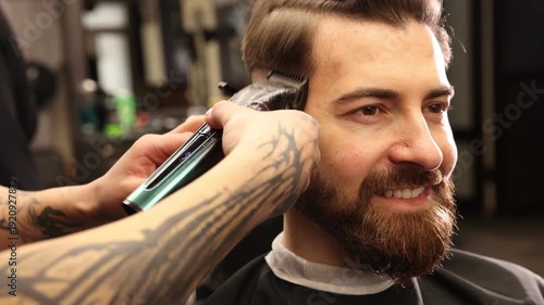 Stylist cutting man's hair with clipper in barbershop, closeup