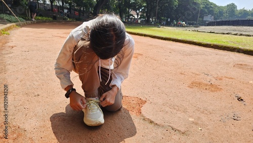 Photos South East Asian runner girl squat and tying her sneaker at jogging track