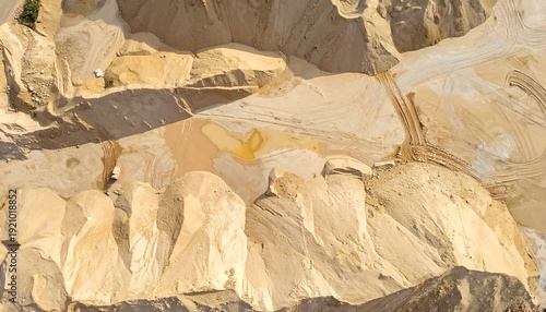 Aerial view of an open sand pit with piles of yellow and light beige sand, showing shadows and water