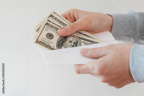 Photos Close up of hands holding a white envelope containing US dollar banknotes