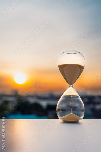 Hourglass with flowing sand against sunset sky background, time management and deadline concept, life passing by or countdown metaphor, sand clock for business productivity.