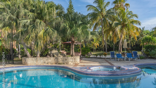 Outdoor swimming pool. A tropical resort. A convoluted shape with rounded edges. Blue tiled bottom. Clear water. Deck chairs, canopy on the terrace. Palm trees, blue sky. Cuba. Varadero. Hotel.