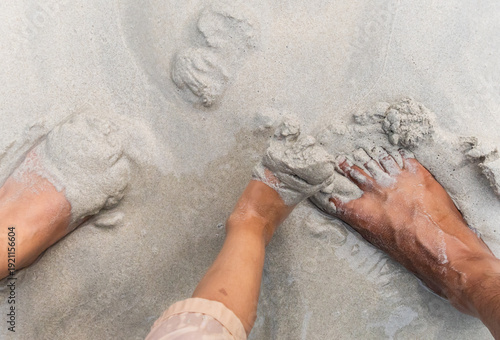 Fotografía child and parent playing with wet sand beside bare feet on beach