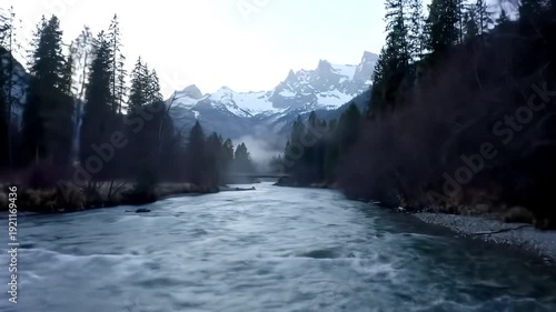 Majestic wide shot of a powerful river flowing through a pristine mountain valley flanked by dense evergreen forests under a bright cloudy sky showcasing the raw beauty of untouched wilderness and na.